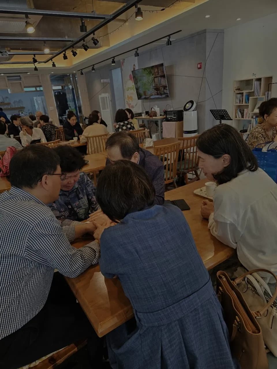 카페 테이블에 모여 서로 손을 맞잡고 기도하는 성도들